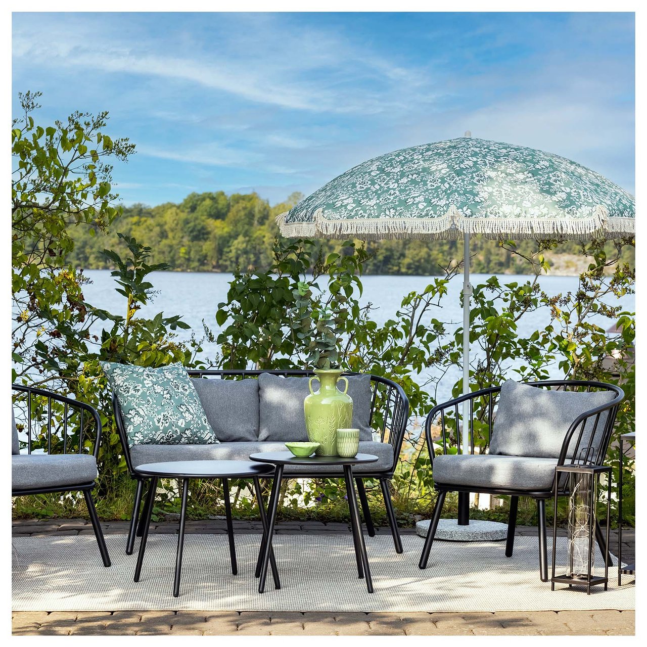 Kompaktes Lounge-Set aus schwarzem Stahl, bestehend aus einem Sofa, zwei Sesseln und einem Tisch. Die Sitzgruppe steht unter einem Sonnenschirm auf einer Terrasse aus Steinplatten.