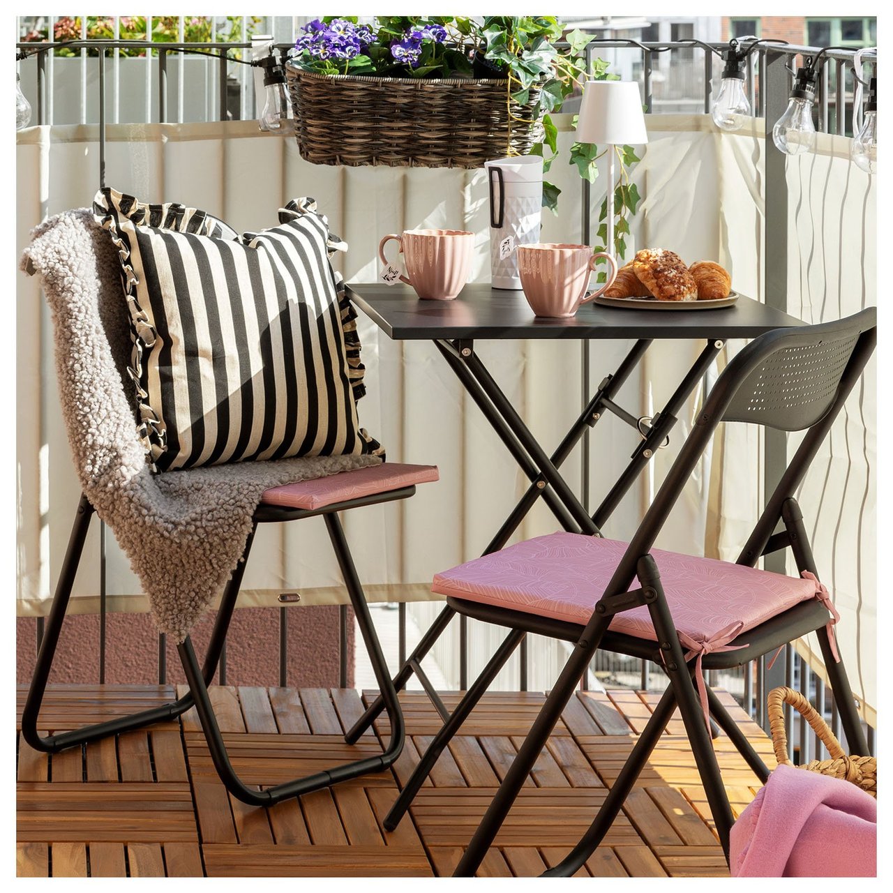 Lite kafésett med to sammenleggbare stoler og bord på en liten balkong med innsynsskjerming.