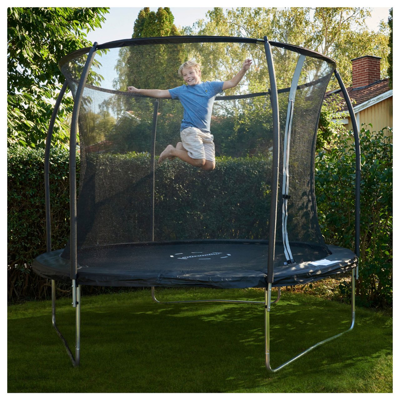 Flicka hoppar högt på en studsmatta i trädgården.