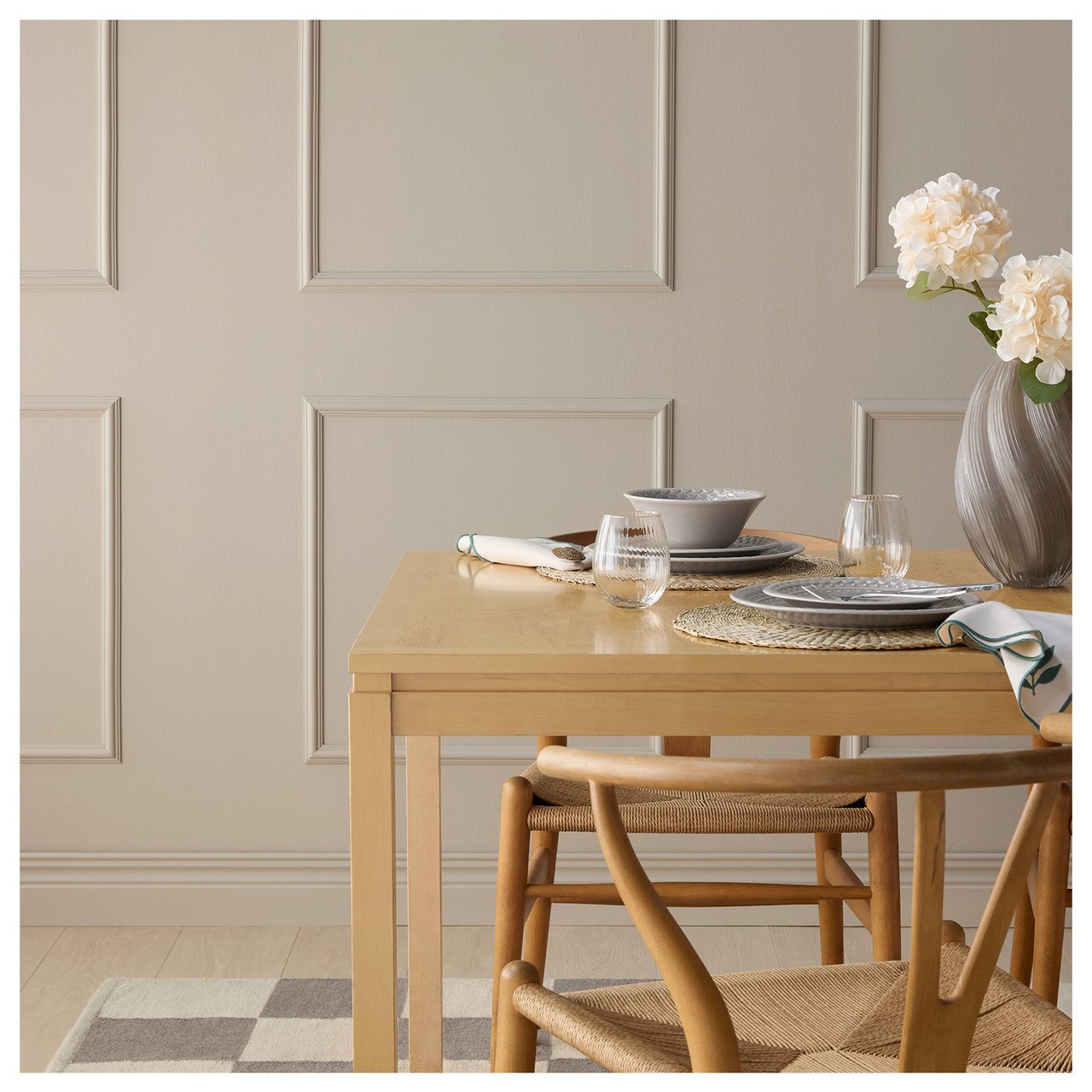 Ett köksbord på en rutig matta framför en grå-beige vägg med rutor av dekorlister.