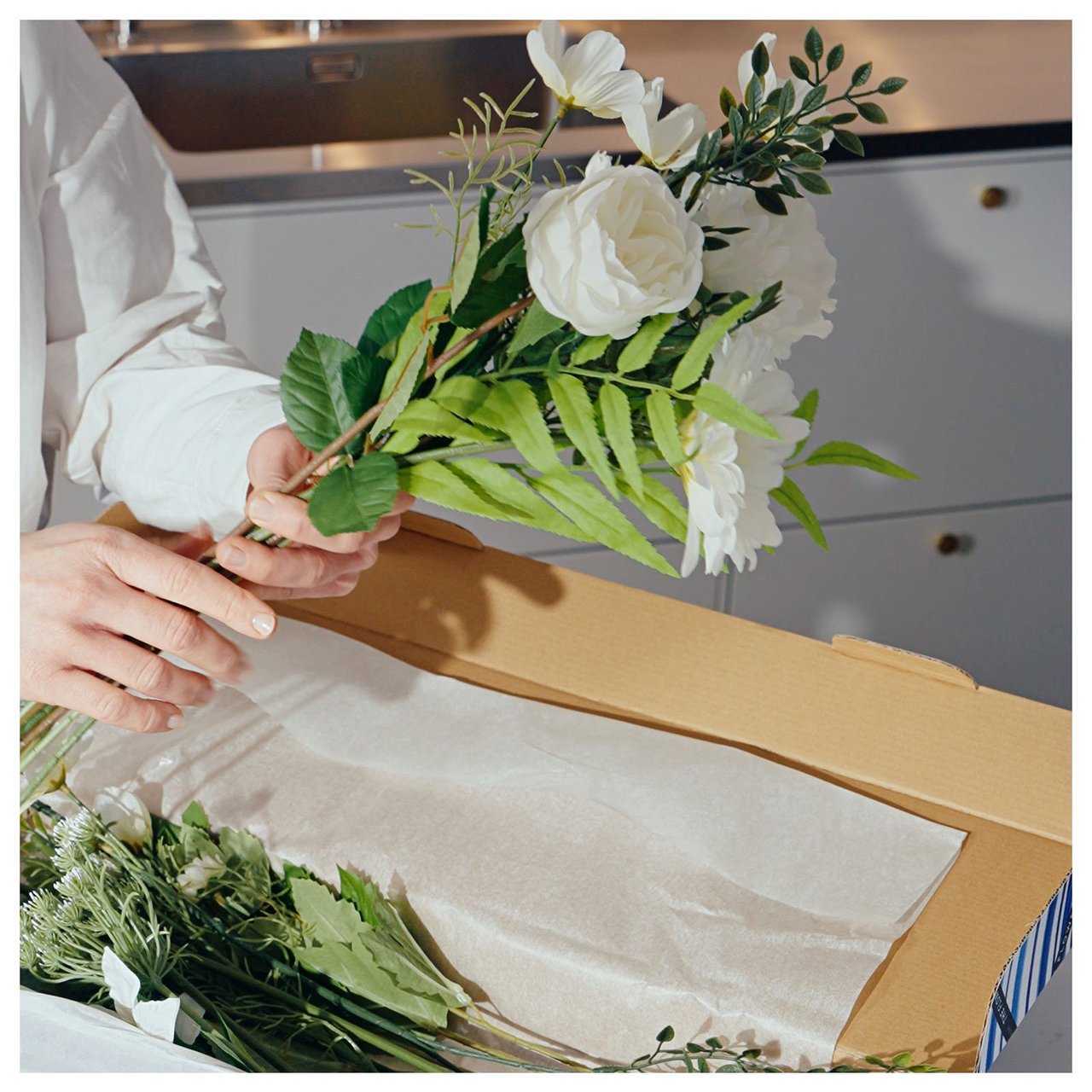 Weiße Kunstblumen werden aus einem Karton ausgepackt.