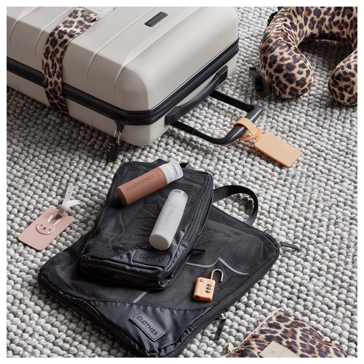 Koffert med pakkekuber, nakkepute og bagasjemerke ligger spredt utover et teppe.