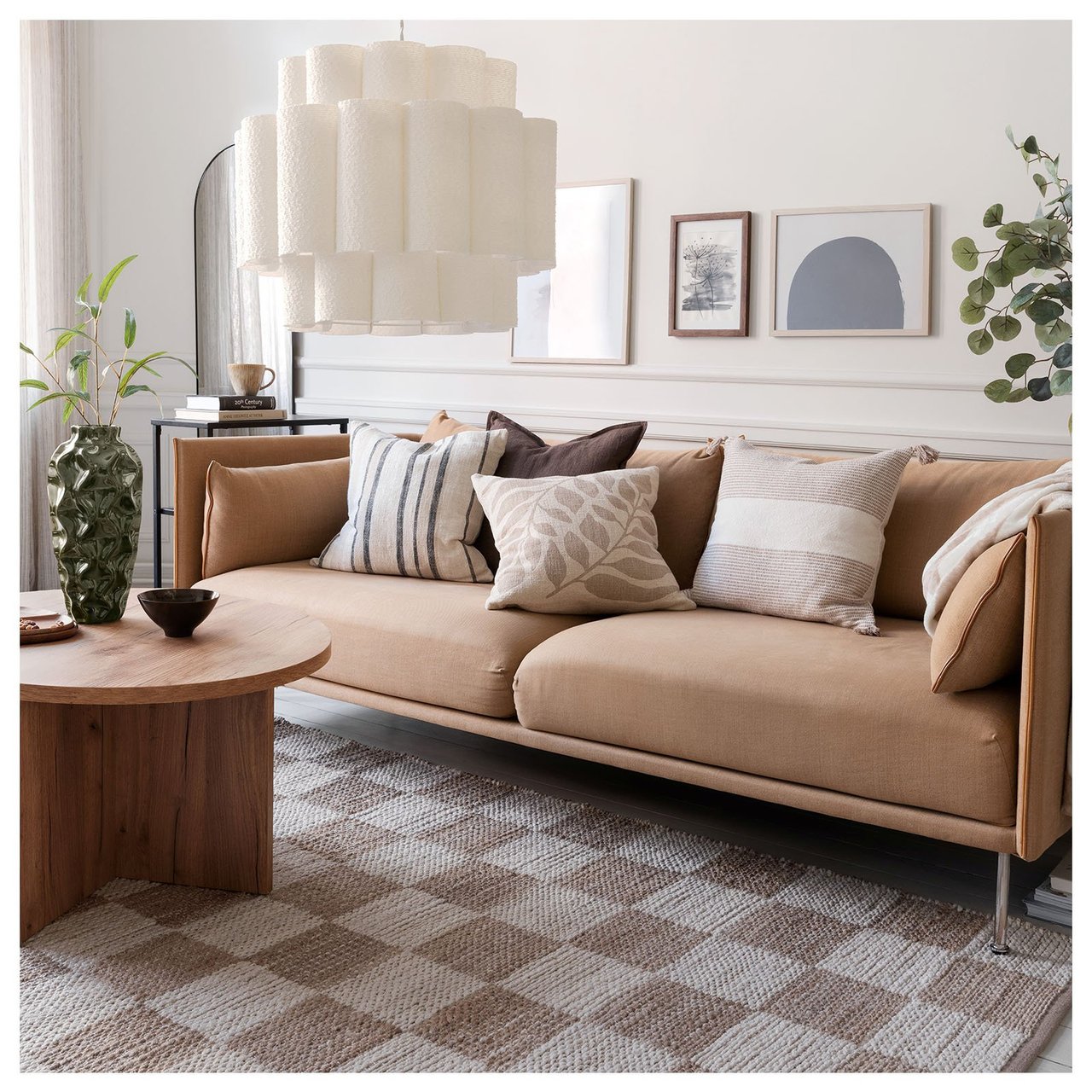 En brun sofa med naturfargede puter står på et rutete teppe i brunt og hvitt i en stue sammen med et trefarget bord.