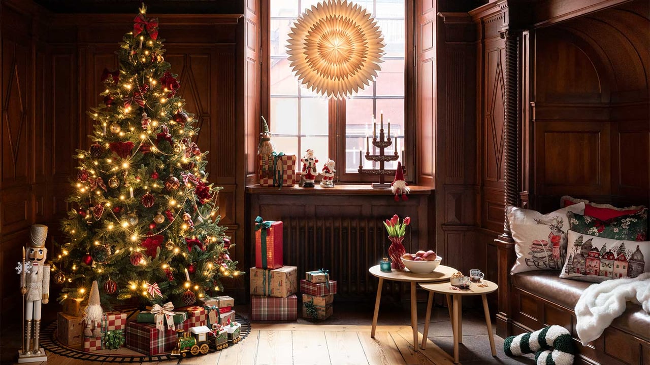 Koristeltu joulukuusi, joululahjoja ja jouluvaloja jouluisessa huoneessa, jossa on adventtitähti ja adventtikynttelikkö.