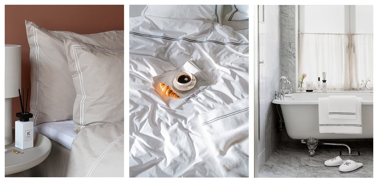Seng med beige sengetøy. Kaffekopp og croissant på en avis i en seng. Hvite håndklær henger over kanten på et badekar.