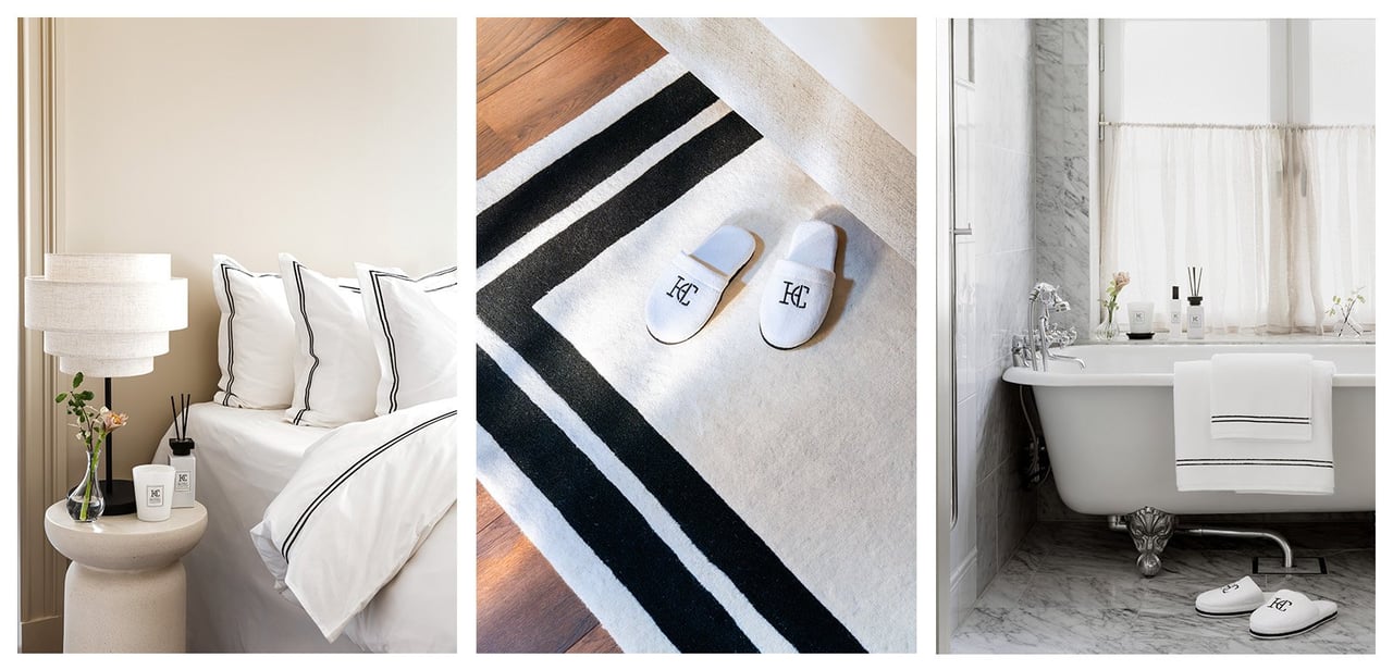 Säng bäddad med vita sängkläder med svarta ränder. Tofflor står på vit matta med svarta ränder. Badrum där vita handdukar hänger över badkar.