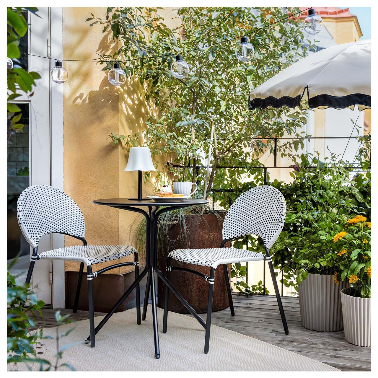 En grønn og frodig uteplass med to stoler, et kafébord og en parasoll.