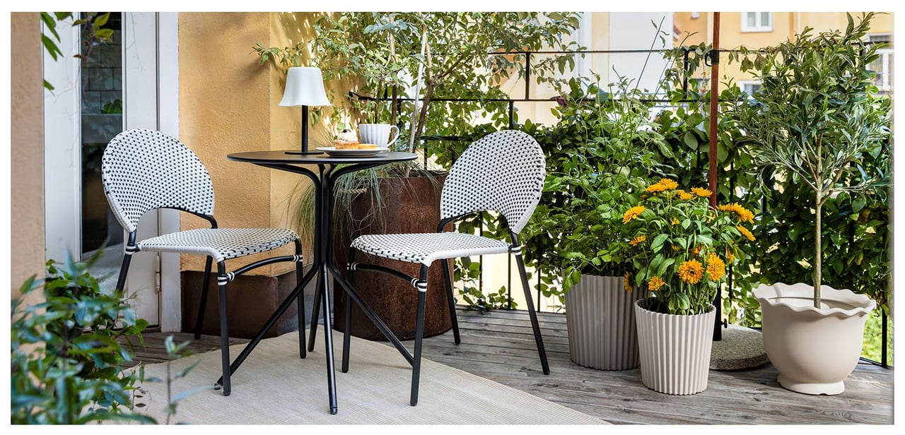 En grønn og frodig balkong med to svarthvite stoler, et kafébord og en svarthvit parasoll.