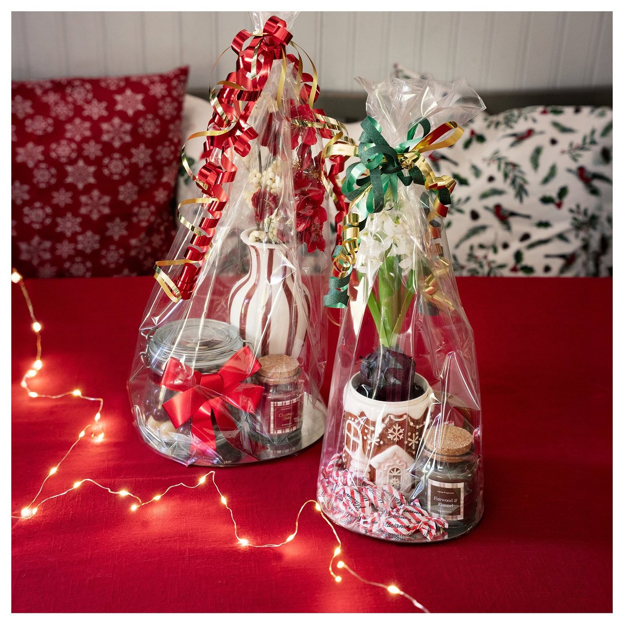 Zwei in Geschenkfolie eingeschlagene Weihnachtsgeschenke mit Dekorationen und kleine Geschenke auf einem roten Tisch.