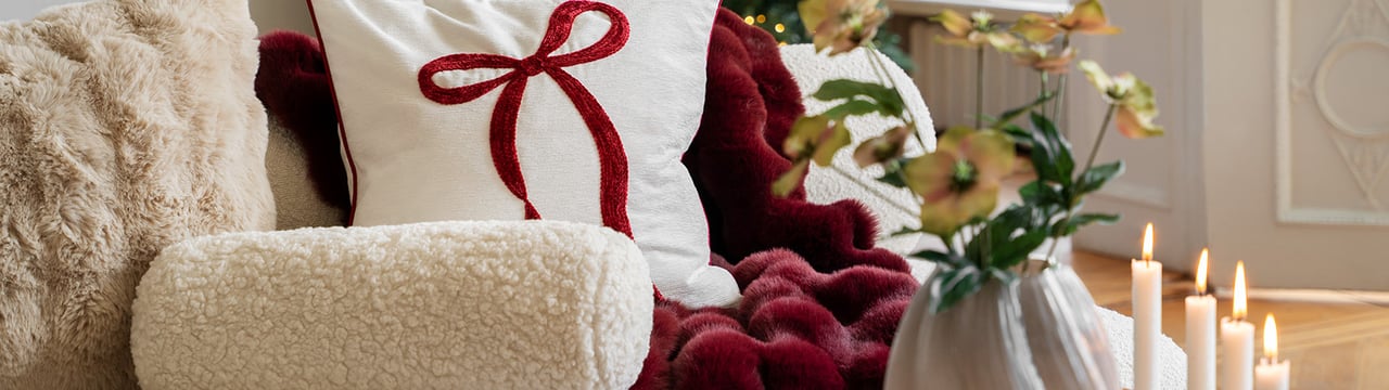 Weihnachtliches Wohnzimmer mit weichen Kissen und Decken in Rot und Weiß sowie dekorativem Weihnachtszug mit Kerzen.