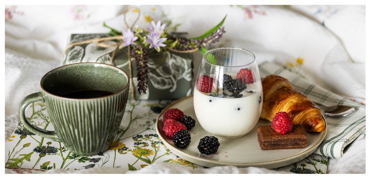 Luxuriöses Frühstück in einem Bett mit Joghurt in einem Glas, Croissant, Beeren, Schokolade und Kaffee.