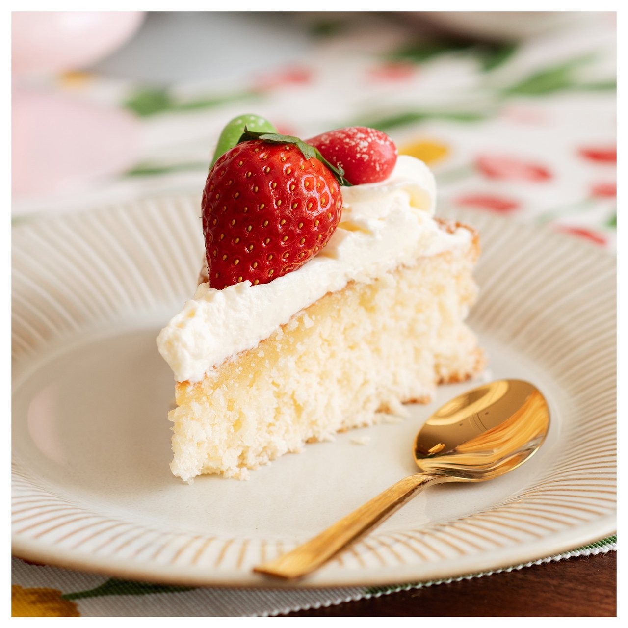 Kuchenstück mit Erdbeeren und Goldlöffel auf einem naturweißen Dessertteller.
