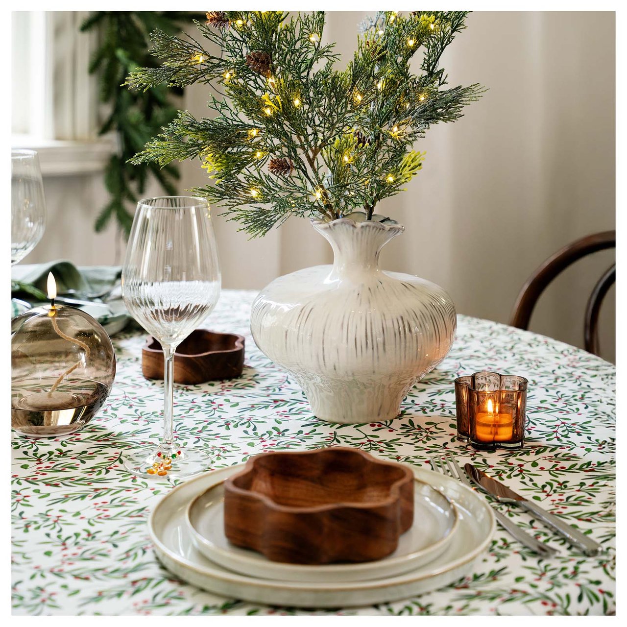 Weihnachtstisch mit grün gemusterter Decke und Vase mit Kiefernzweigen.