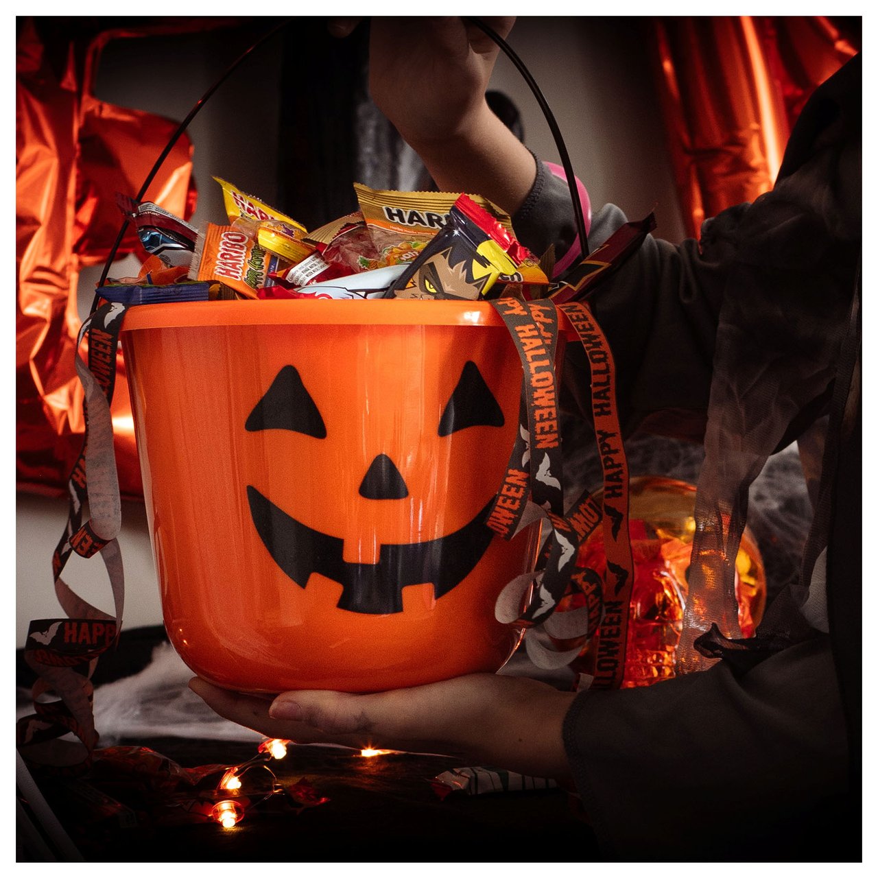 Person som holder en bøtte som forestiller et halloween-gresskar fylt med godteri.
