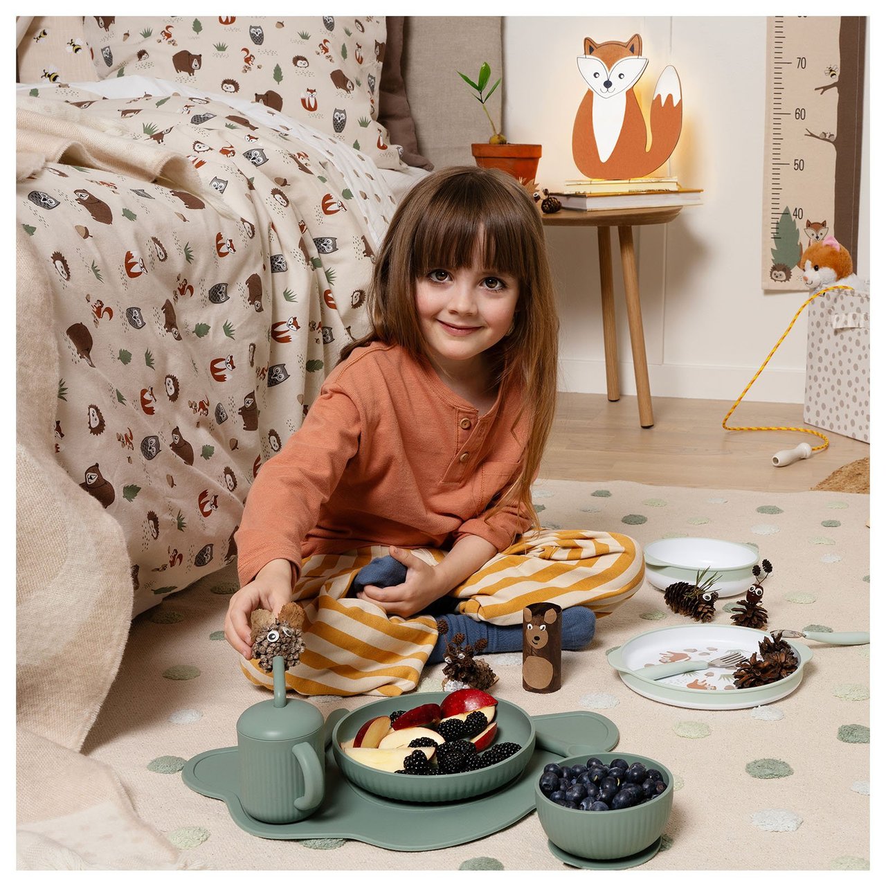 Ein Kind spielt mit einem grünen Kinderservice auf dem Boden eines Kinderzimmers.