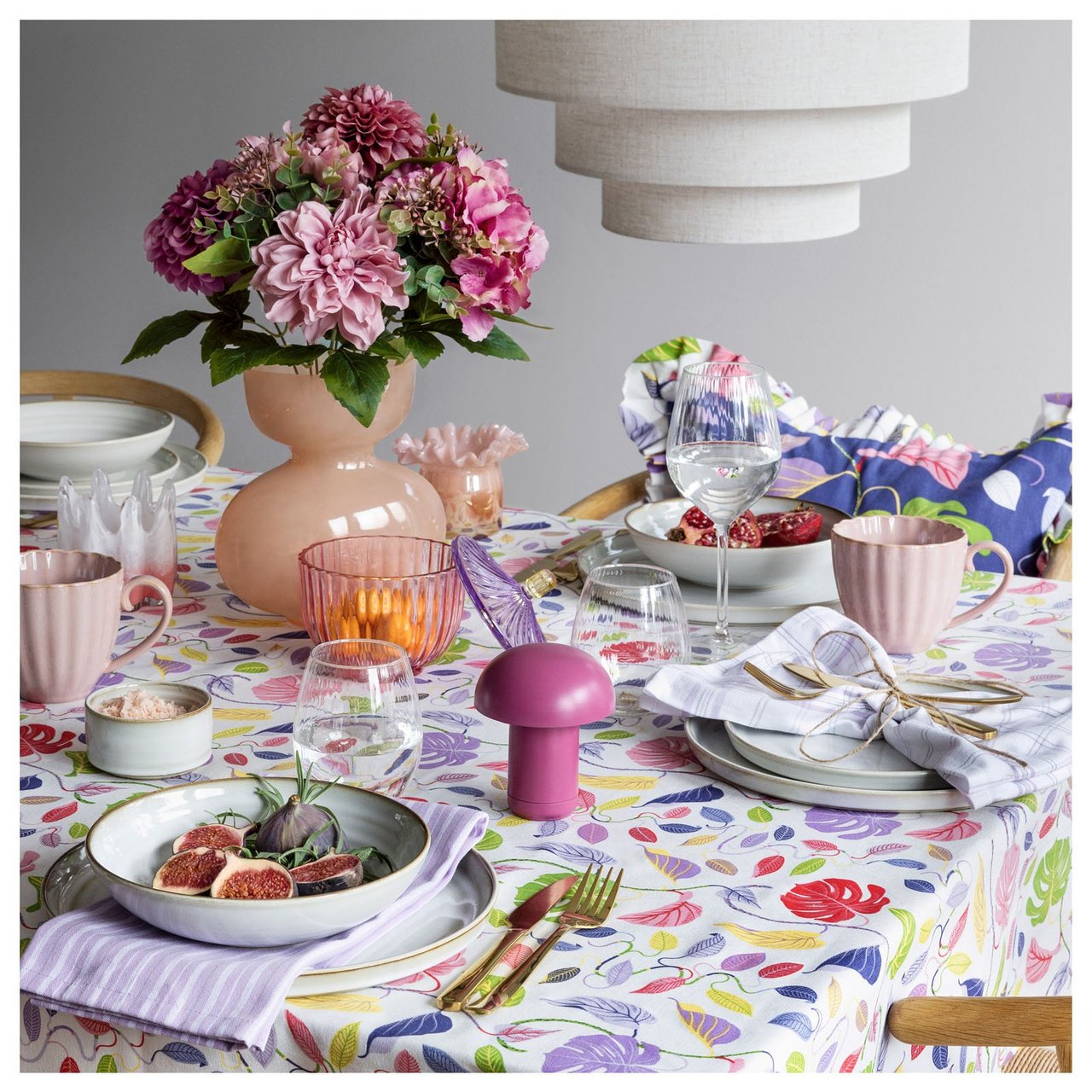 Värikäs katettu pöytä, jolla on kukkia, astioita ja tekstiilejä inspiroivassa päivälliskattauksessa.