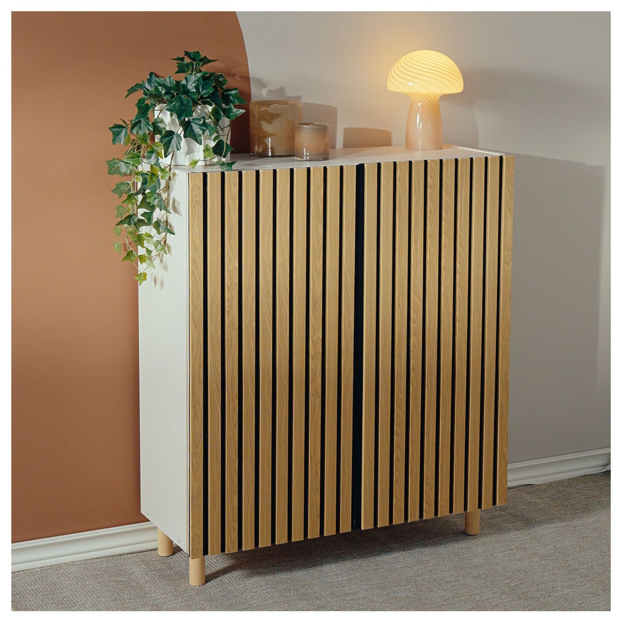 Ett skåp med dörrar klädda i akustikpanel står mot en vägg med dekorativa detaljer ovanpå.