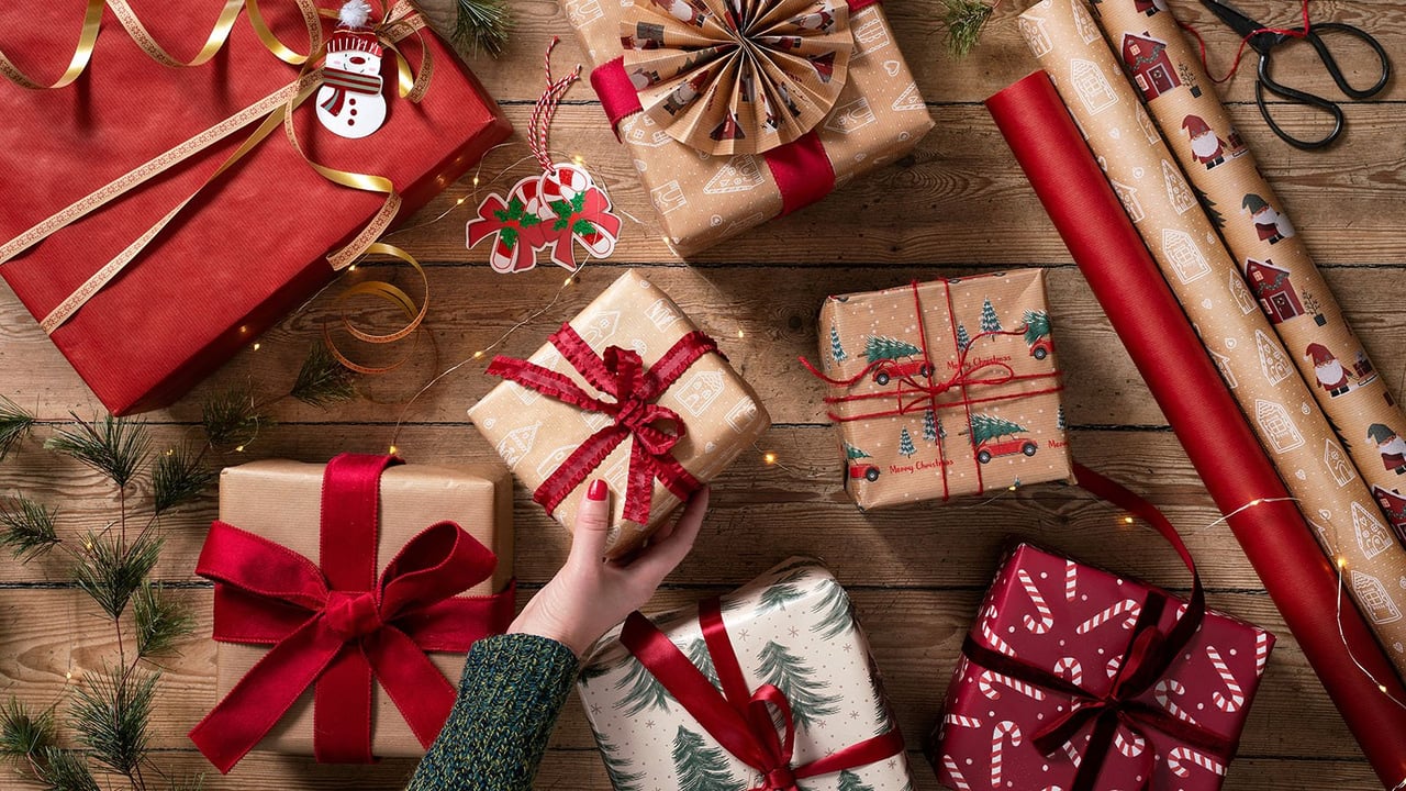 Weihnachtsgeschenke in rotem und braunem Papier mit Schleifen und Deko auf einem Holzboden.