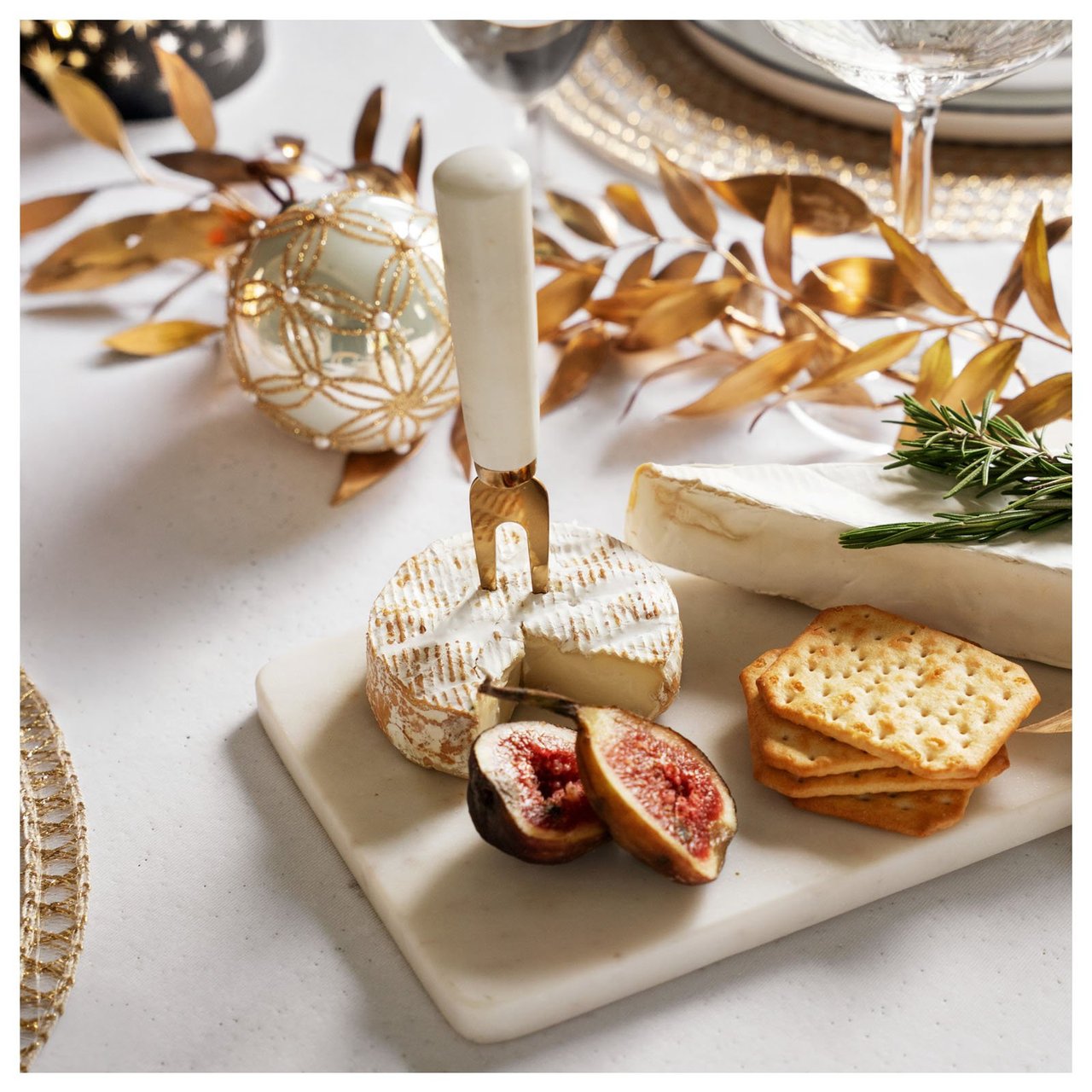 Ostbricka med kex, fikon och ost på ett festligt dukat bord.