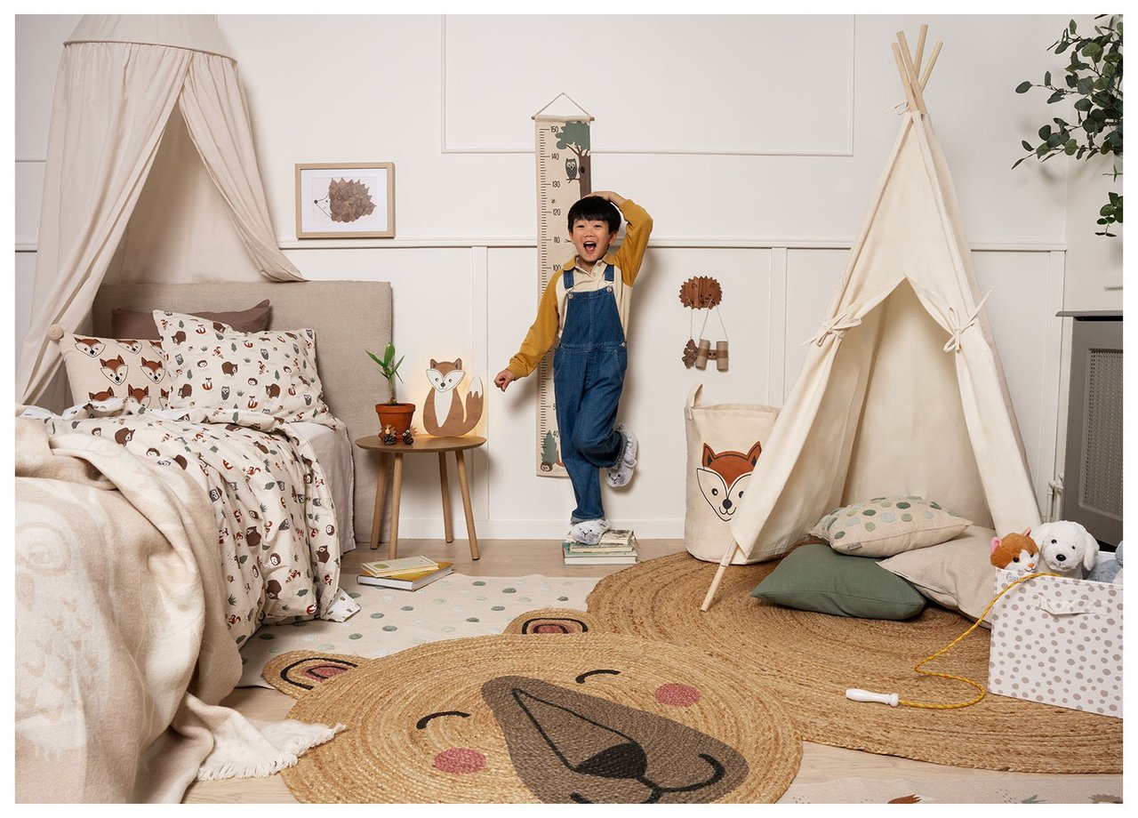 Kinderzimmer in schlichten Farben mit Bett und Tipi sowie Teppich mit Bärenmotiv. Ein kleiner Junge steht an einer Messlatte und misst sich.