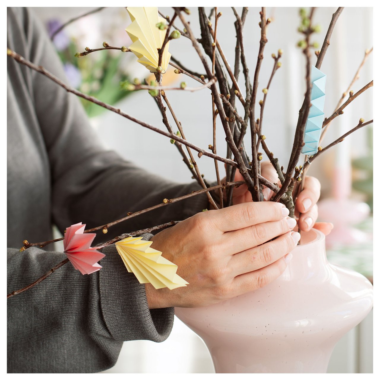 Person, die Osterzweige mit Schmuck in einer rosa Glasvase anordnet.
