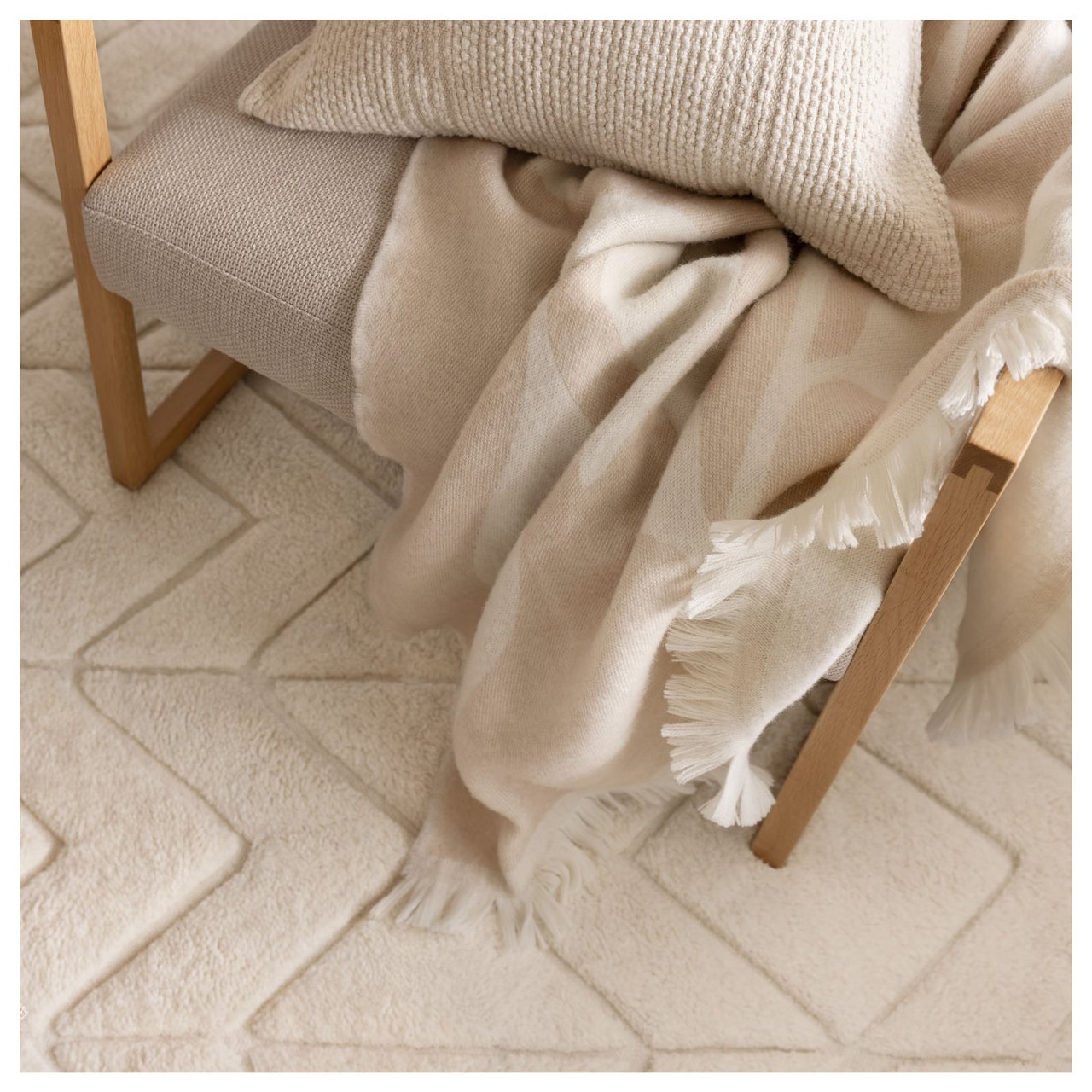 Ein Sessel mit einer hellbeigen Decke und einem Kissen steht auf einem naturweißen Teppich. 