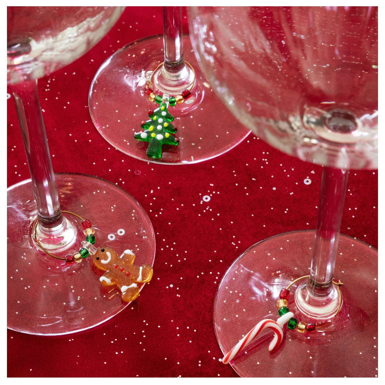 Drinkmarker mit Weihnachtsmotiv an Weingläsern auf rotem Glitzertuch.