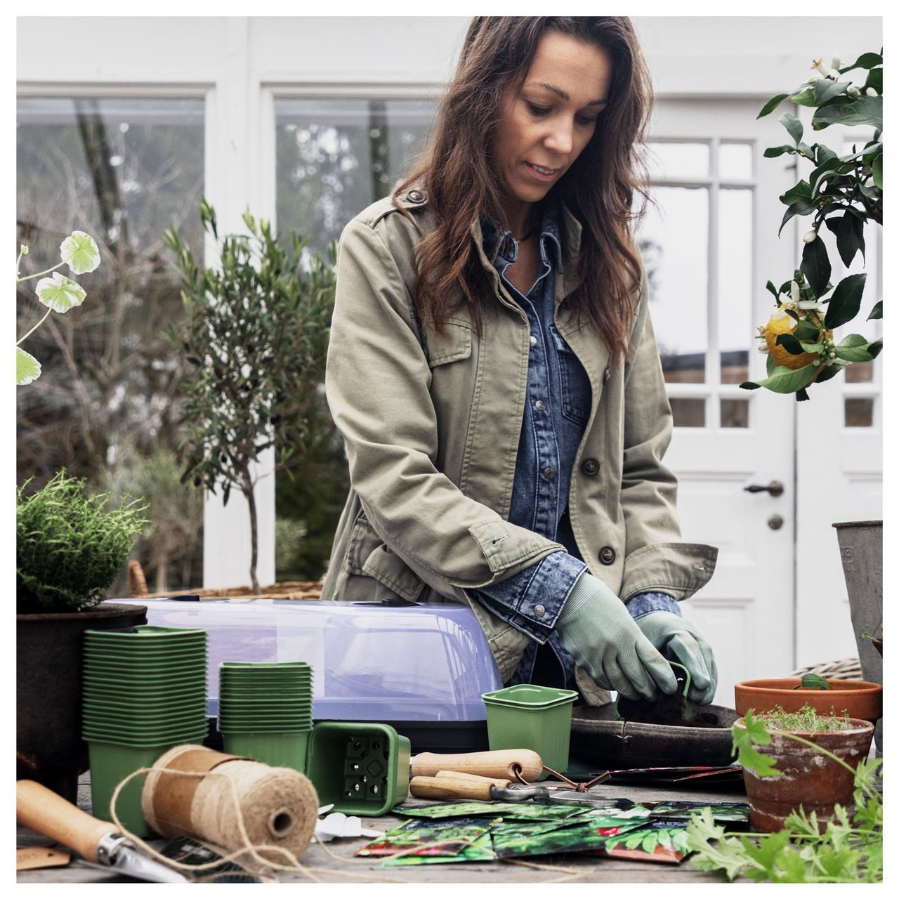 Sofia står i drivhuset sitt ved en benk og planter i en plastpotte.
