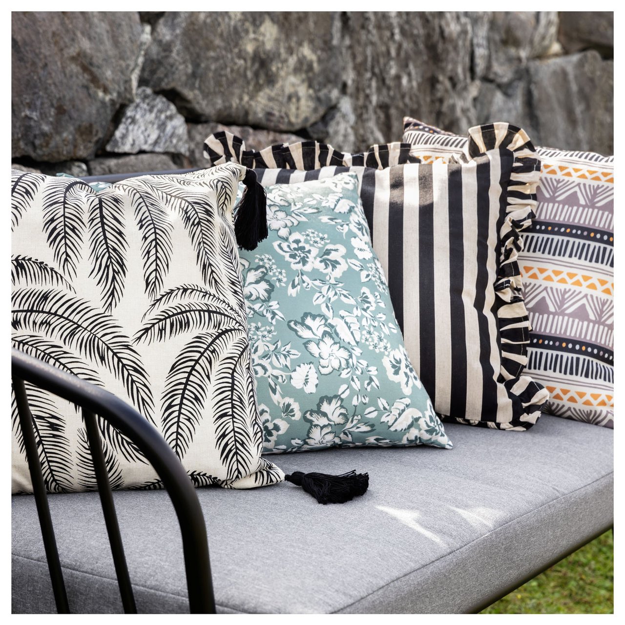 Mehrere gemusterte Kissen auf einem Outdoor-Sofa, das in einem Garten steht.