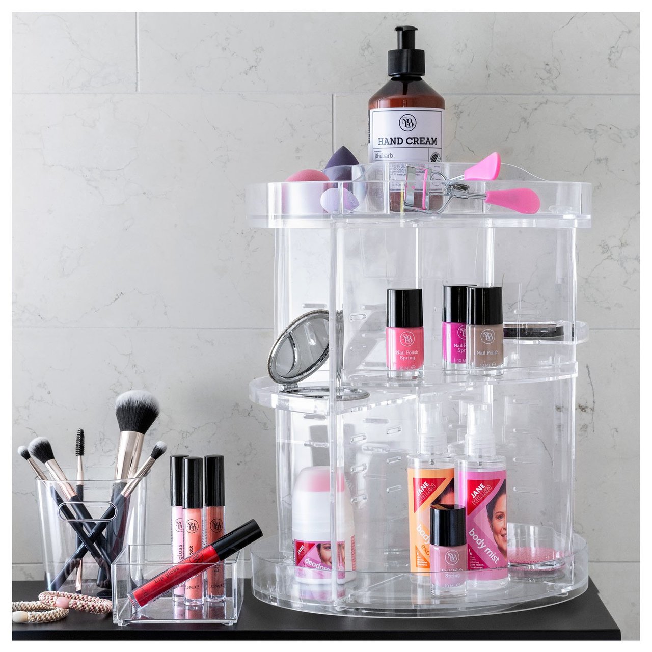 Meikki- ja ihonhoitotuotteet järjestettynä läpinäkyvään, käännettävään säilytystelineeseen kylpyhuoneen kaapissa.
