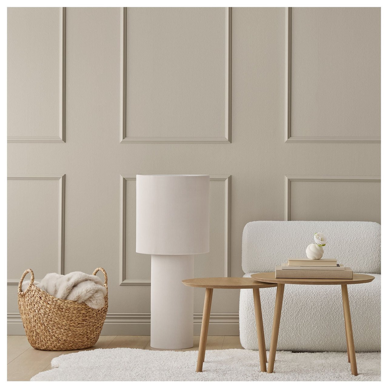 Ett rum med grå-beige väggfärg. Framför väggen står en korg, en golvlampa och ett bord. På golvet ligger en vit matta.