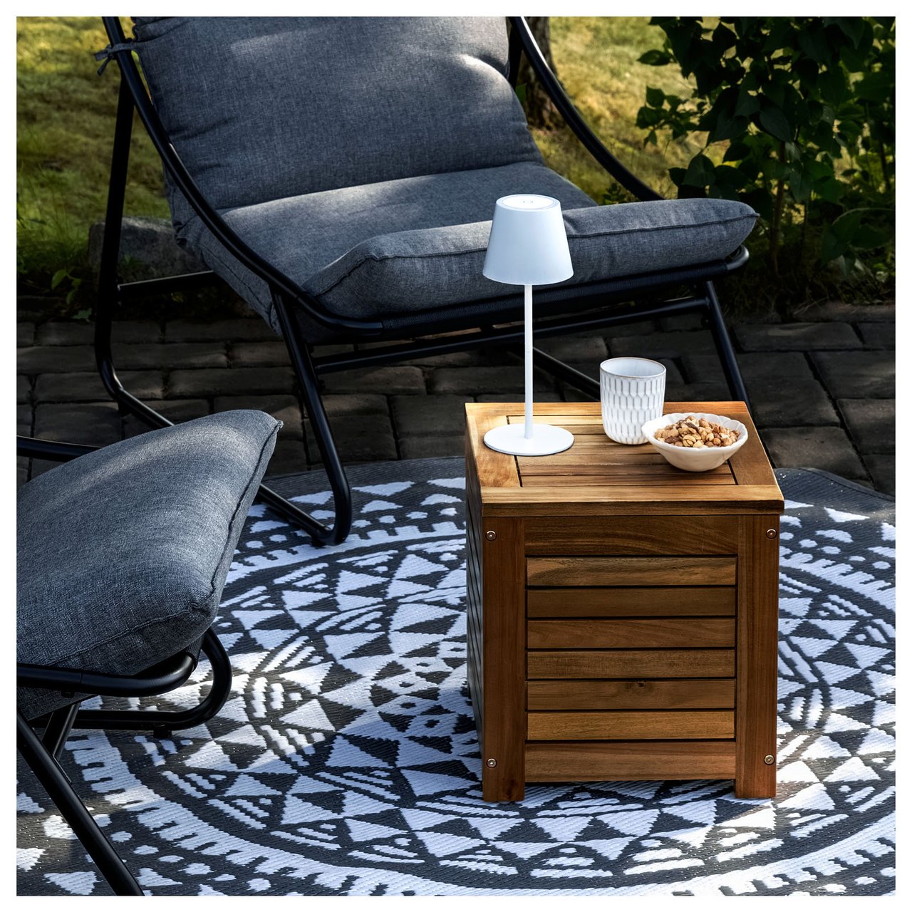 Gemütliche Ecke einer Terrasse mit zwei Sesseln und einem Tisch mit einer von Solarzellen betriebenen Lampe.