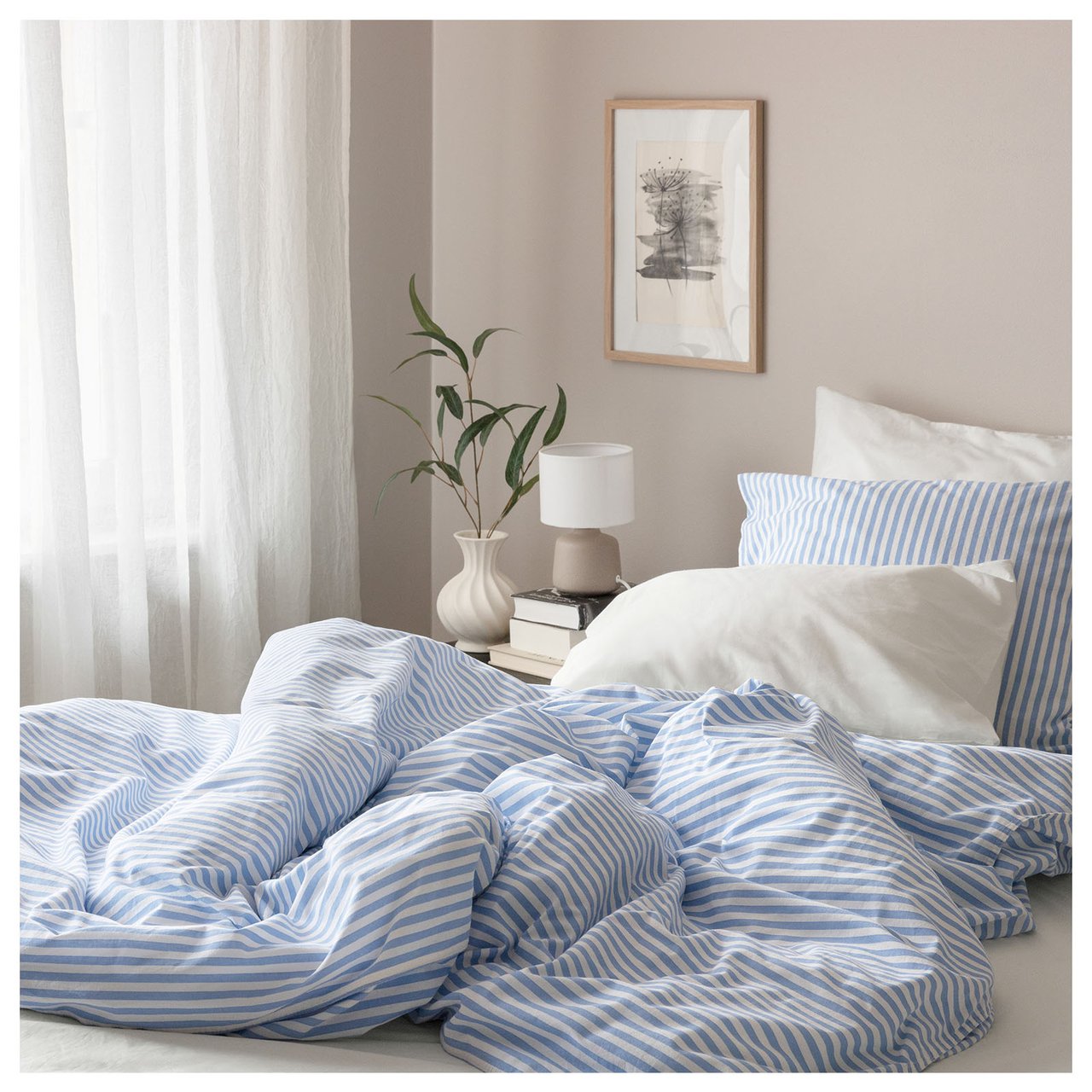 Sovrum med blåvitrandiga sängkläder och vita gardiner.