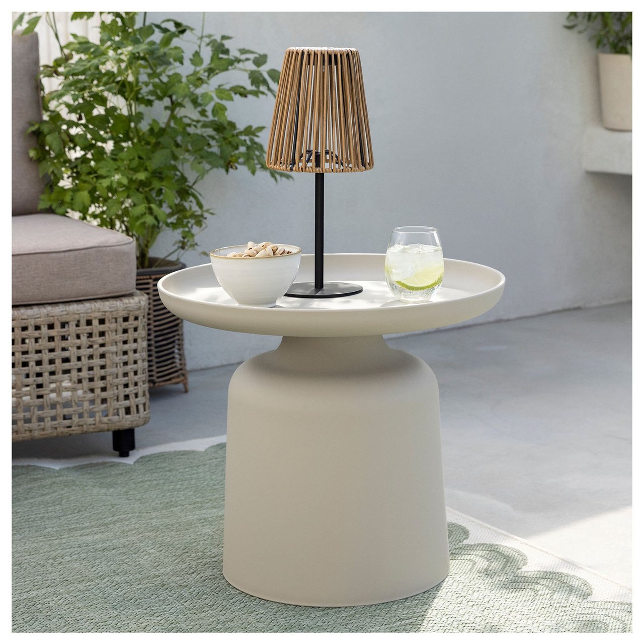 En bordlampe i rotting står på et lite bord på en uteplass.