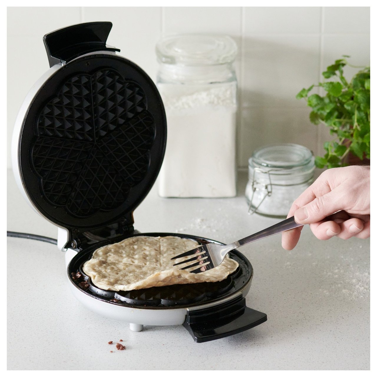 Runde Waffel, die mit einer Gabel in einem Waffeleisen gedreht wird, in einer Nahaufnahme.