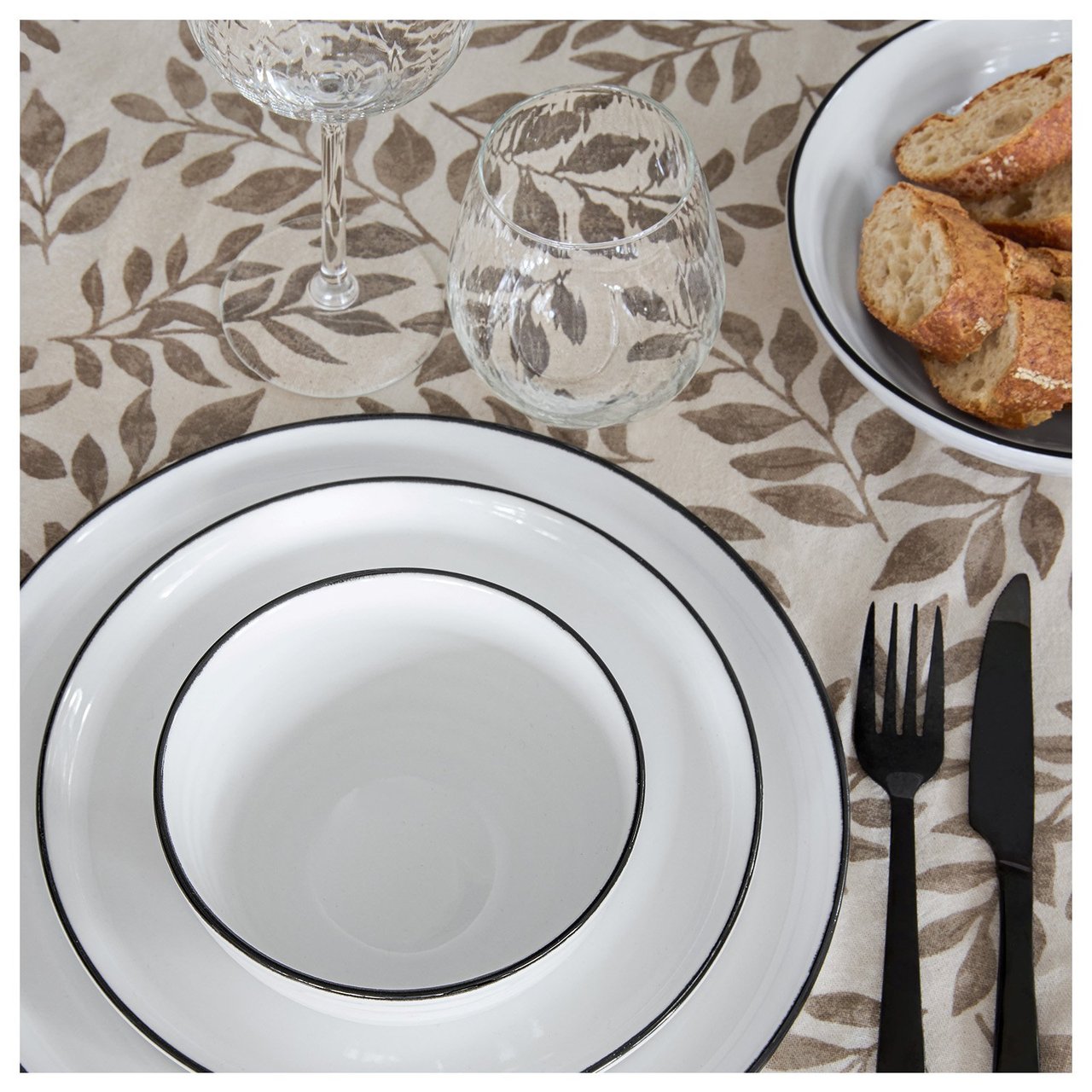 Weiße Teller auf einer Tischdecke mit Blattmuster.