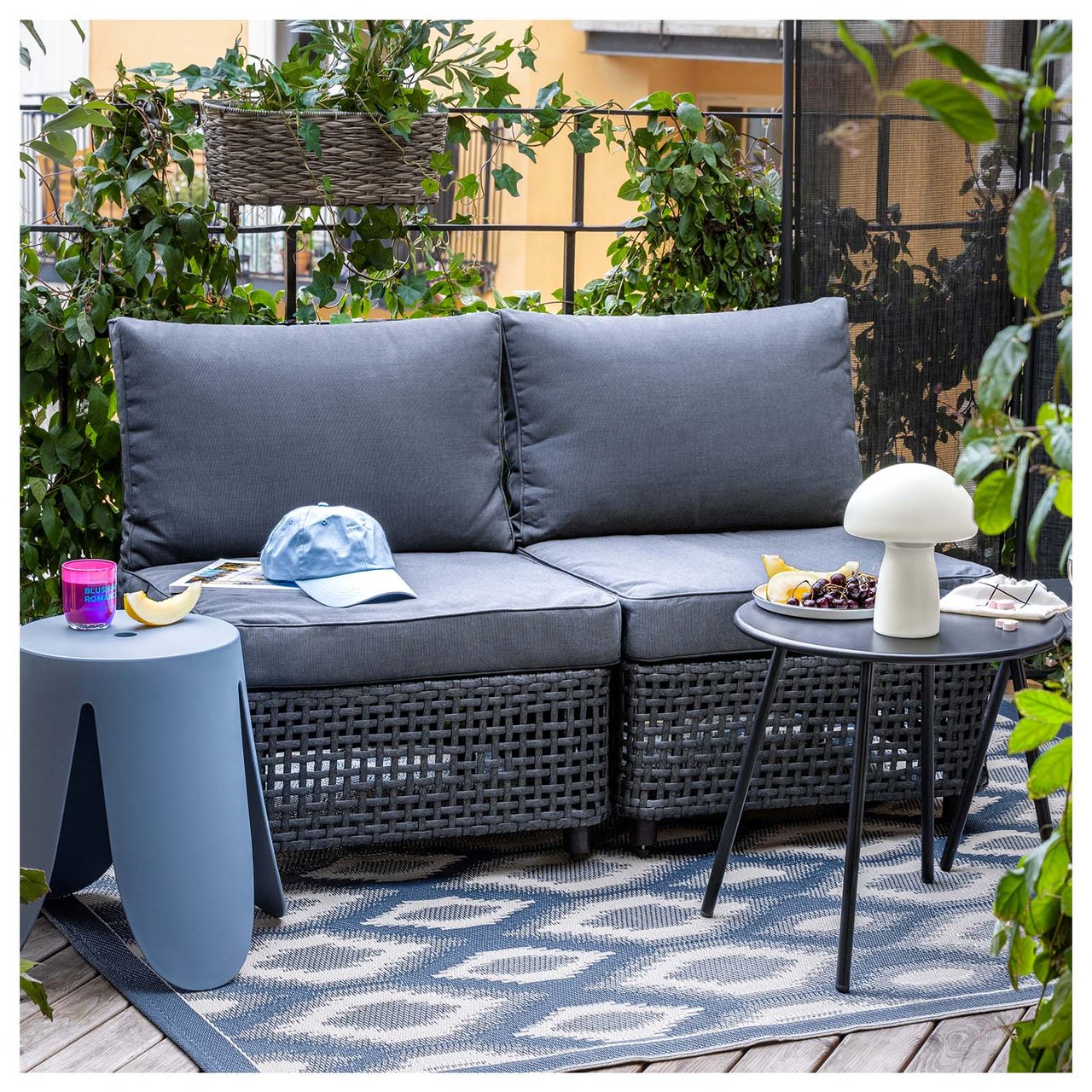 Balkong med svart loungesofa og blått teppe med mønster.