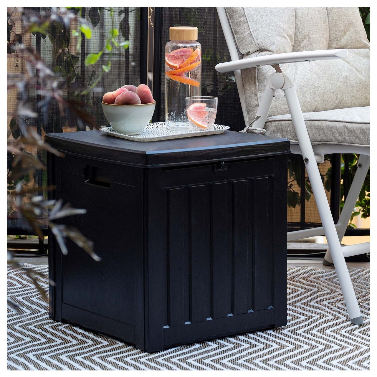 Liten kvadratisk oppbevarings- og putekasse i svart plast som brukes som avlastningsbord på balkong.