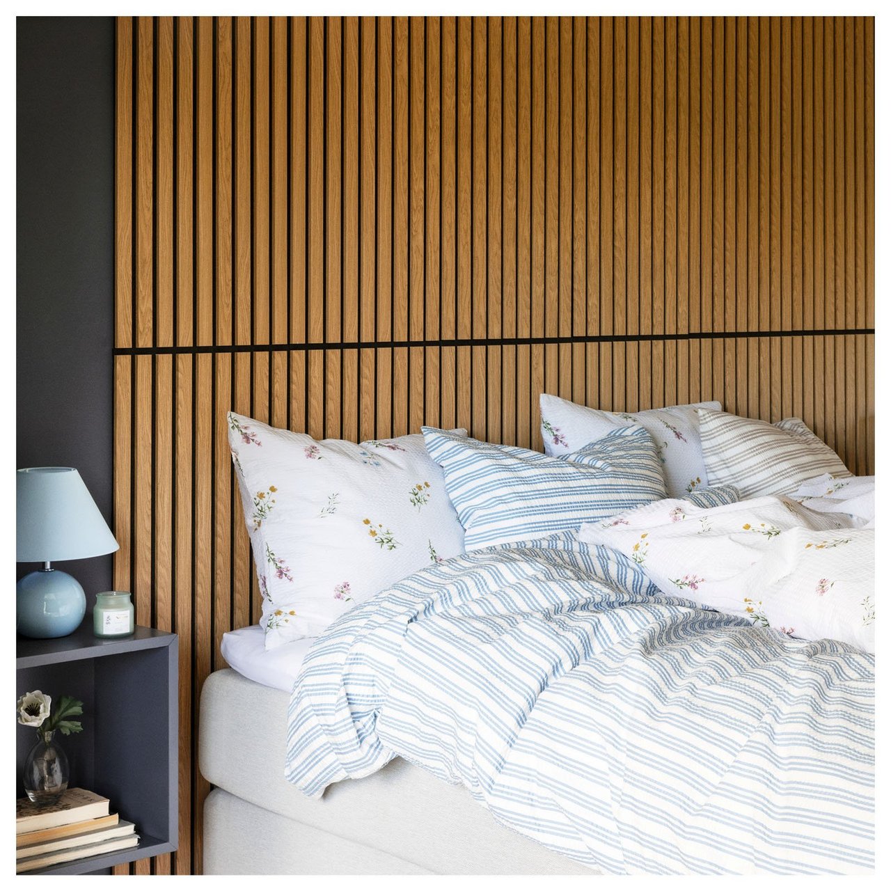 Makuuhuone, jossa on sänky ja siinä kuviolliset vuodevaatteet akustiikkapaneelista valmistettua seinää vasten.