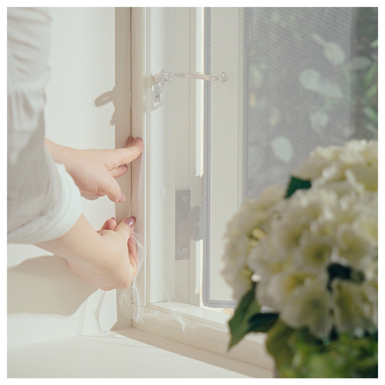 En person setter opp myggnett for et åpent vindu.