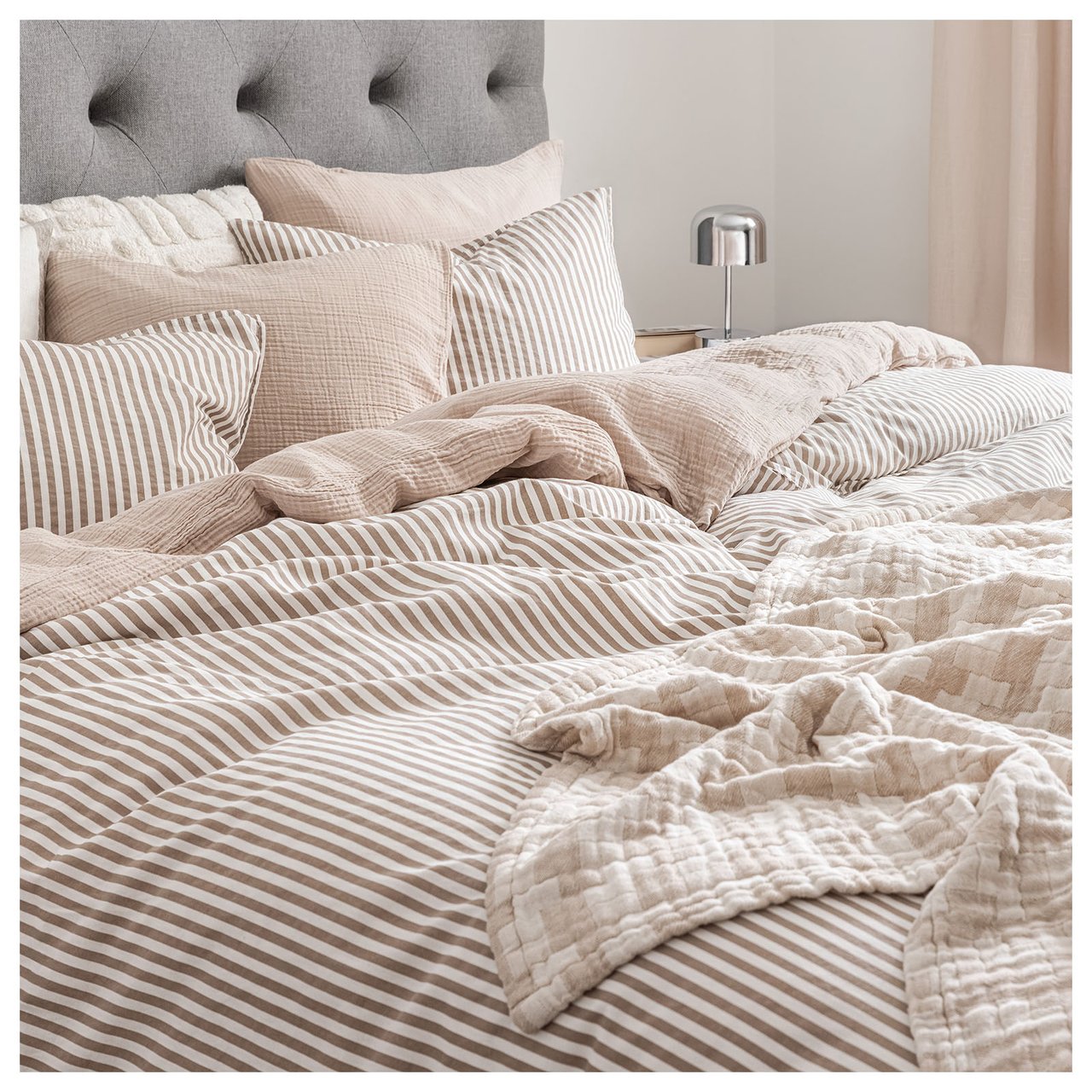 Bett mit gestreifter Bettwäsche in Beige und mehreren Kissen.