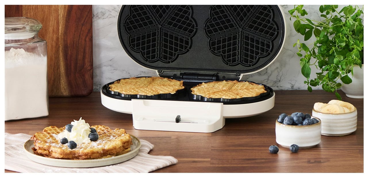 En hög med våfflor på en tallrik. Sylt, bär, vispgrädde och en kopp kaffe bredvid.