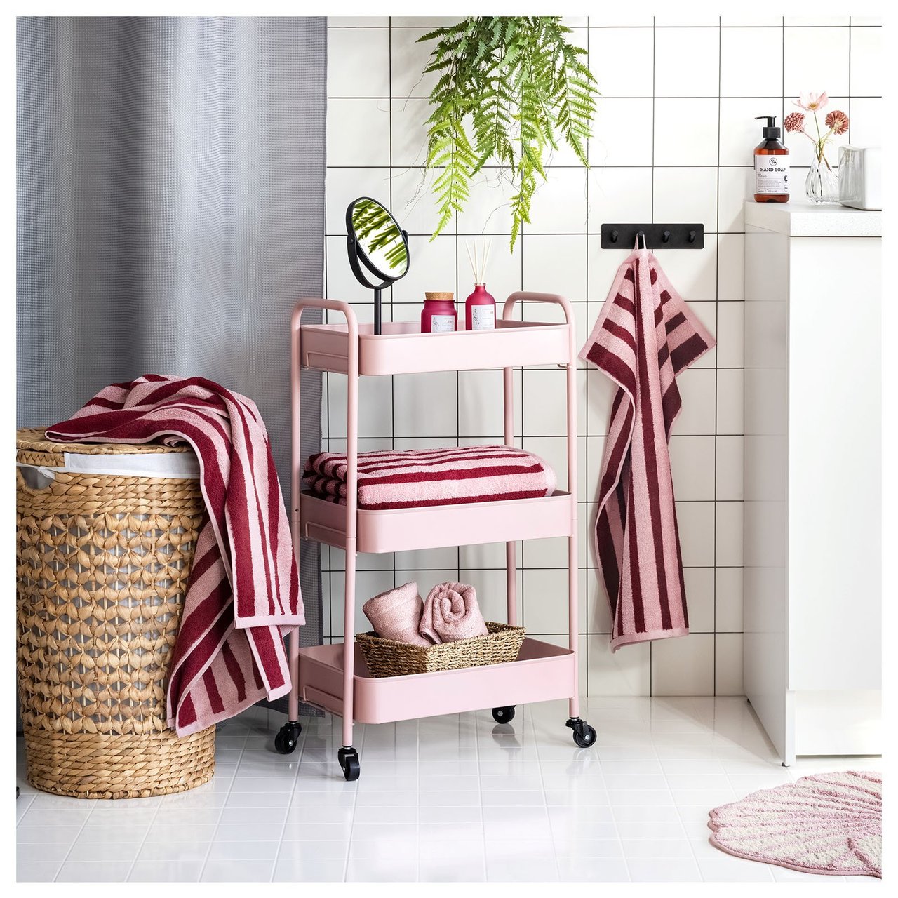 Badezimmer mit rosa Rollwagen, Badematte und rosagestreiften Handtüchern.