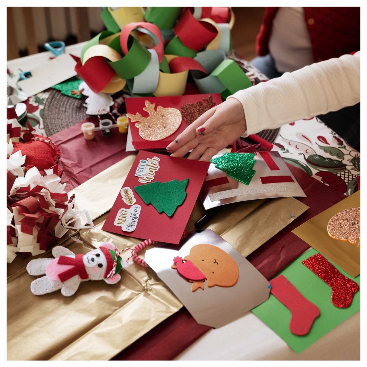 Eine Kinderhand greift nach einer Weihnachtskarte auf einem Tisch voller Weihnachtsbasteleien.