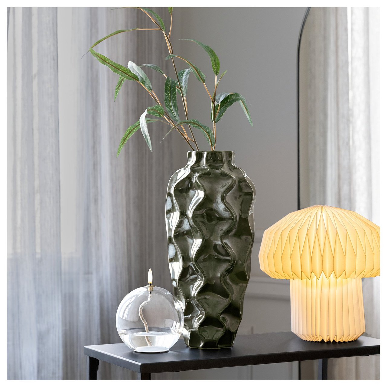 Grønn høy vase med bølgemønster med en grønn kvist i.