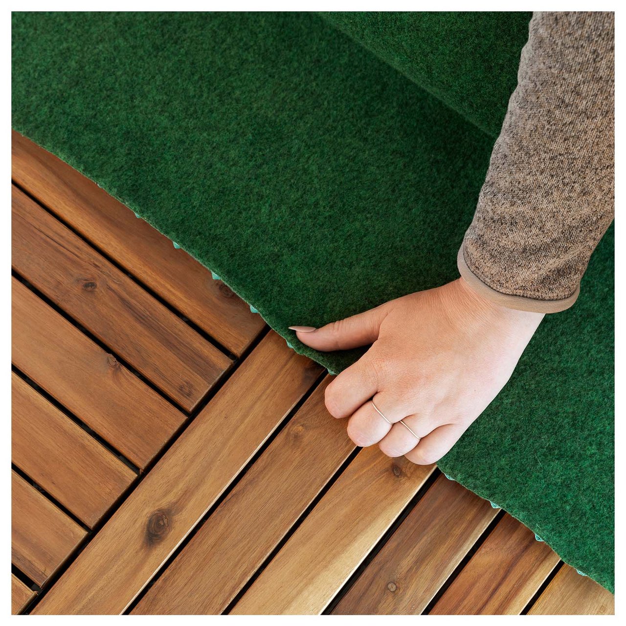 Nærbilde av en hånd som legger et grønt teppe på en treterrasse.