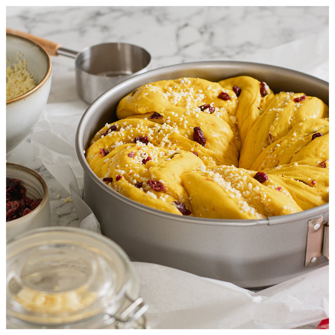 Safranteig, der mit Rosinen und Zucker dekoriert ist, steht in einer Backform zum Backen bereit.