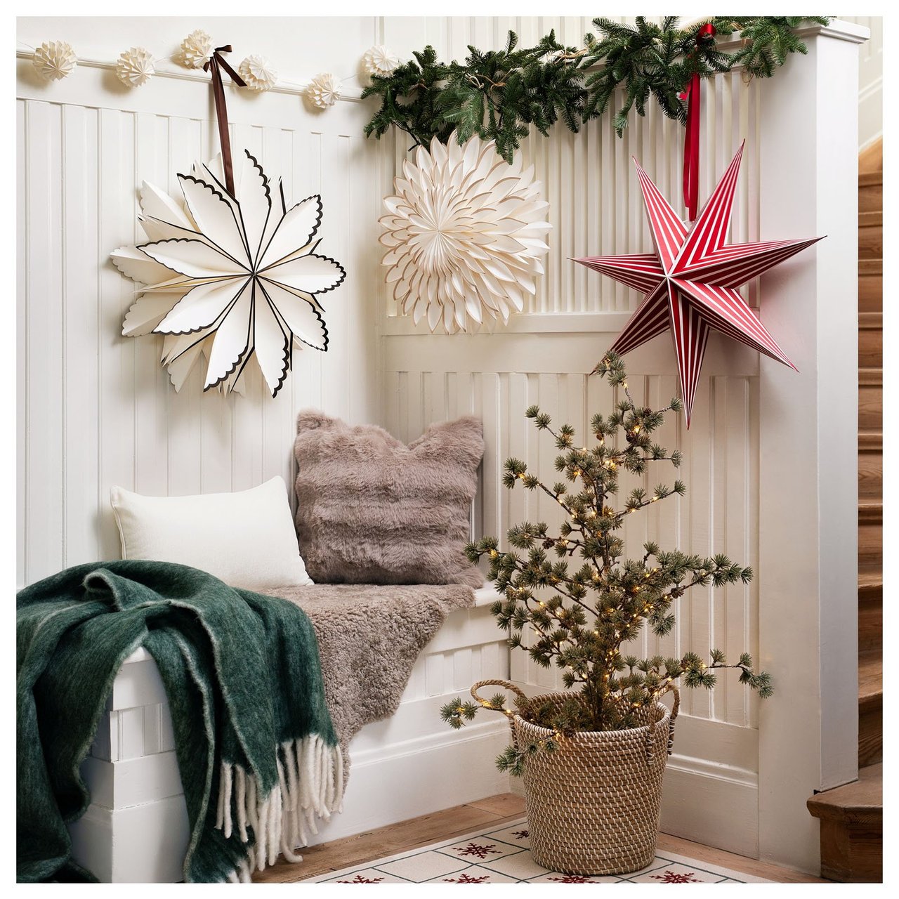 Jouluaiheinen eteinen, jossa tähtiä, pehmeitä tekstiilejä ja pieni kuusi luomassa kutsuvaa tunnelmaa.