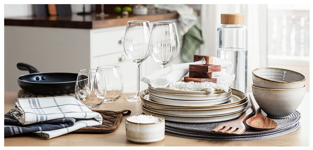 Uppdukad köksbänk med glas, tallrikar, bestick, servetter, stekpanna och kökstillbehör.