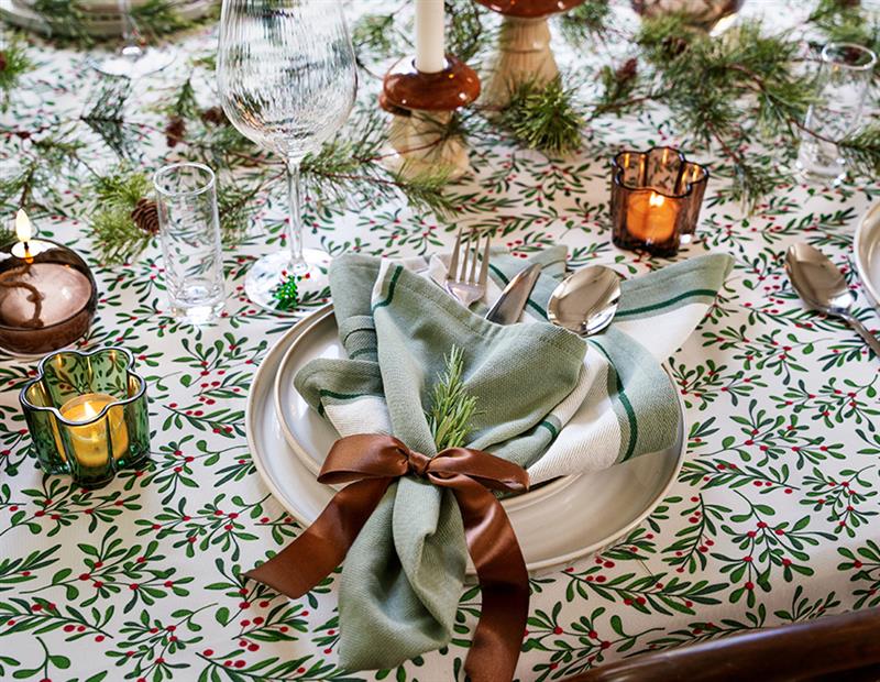 Joulukattaukseen katettu ruokapöytä, jossa lautanen, pellavaservetti, lasi ja kynttilöitä.